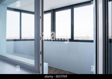 Bright indoor shot showing a balcony with large windows overlooking a cityscape. The door is slightly ajar Stock Photo