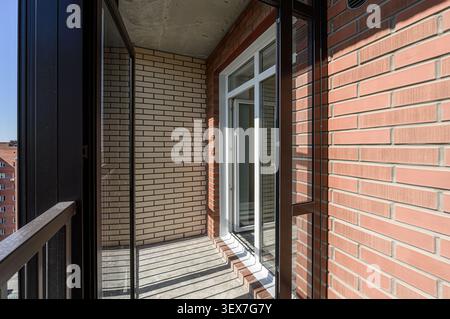 balcony with brick walls, an open white-framed window, and black metal frames. Sunlight casts shadows on the floor Stock Photo