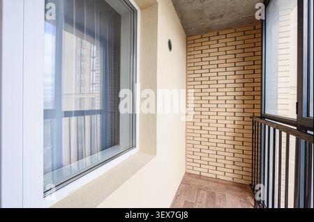 Interior balcony with brick wall, cream wall, wooden floor, and window with white frame. Stock Photo