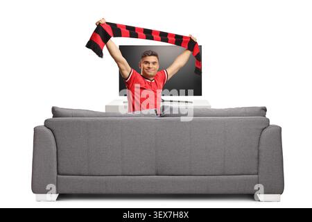 Young man cheering with a scarf behind a sofa in front of a tv isolated on white background Stock Photo