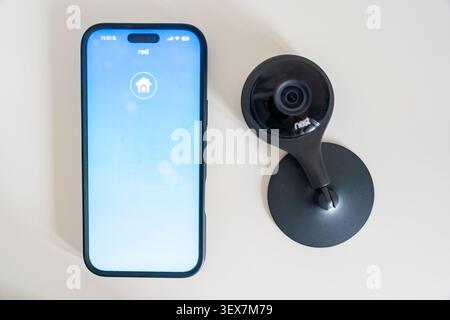 Prague, Czech Republic - June 30, 2026: Smartphone with the Nest app is displayed next to a Nest security camera on a white surface. Smart home Stock Photo