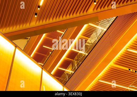Modern architectural interior featuring abstract wooden geometric ceilings and warm linear lighting. Stock Photo