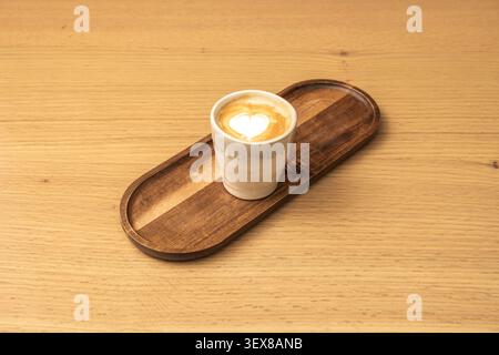Creamy cappuccino featuring a delicate white heart-shaped latte art design served in a small rustic ceramic cup resting on an oval wooden tray atop a Stock Photo