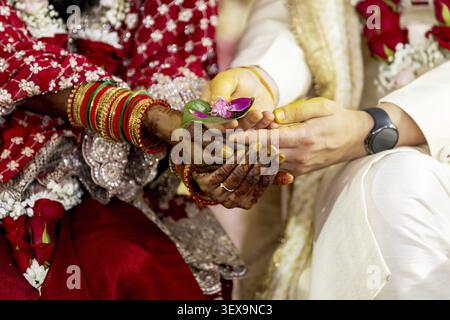 A bride and groom participate in a traditional Indian wedding ritual, holding hands with turmeric paste and flower petals Stock Photo