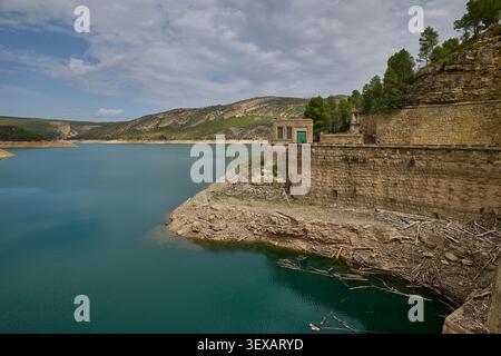 Turquoise reservoir water bordered by layered rocky cliffs and dry shoreline in a mountainous region. Stock Photo