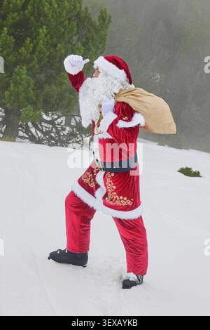 Santa Claus with a bag of gifts looks the road in a snowy foggy forest. Stock Photo