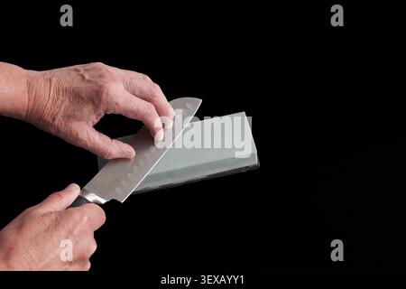 Hands sharpen a knife on a whetstone. Motion captures precision and care. Dark background emphasizes the action. Focus on skill and maintenance. Ideal Stock Photo
