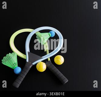 Brightly colored sports gear rests against a dark surface. Tennis rackets and shuttlecocks lie scattered with balls. No people are present. Ideal for Stock Photo