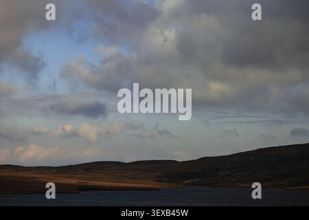 Storr area, Isle of Skye, Scotland, shows dark moorland beside water, layered clouds, and a blue break in the sky above, dramatic outdoor scene view. Stock Photo