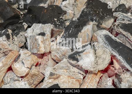 Close-up of glowing charcoal embers covered with white ash and black burned wood, creating a detailed natural fire texture for barbecue, grilling and Stock Photo