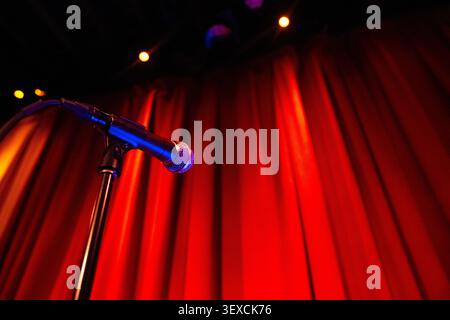 A dramatic cinematic view of a microphone on stage with a red curtain background, spotlights shining down. Stock Photo