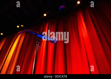 A dramatic cinematic view of a microphone on stage with a red curtain background, spotlights shining down. Stock Photo