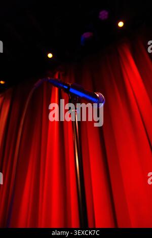 A dramatic cinematic view of a microphone on stage with a red curtain background, spotlights shining down. Stock Photo