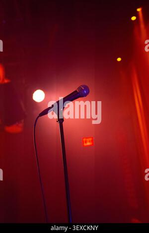 A dramatic cinematic view of a microphone on stage with a red curtain background, spotlights shining down. Stock Photo