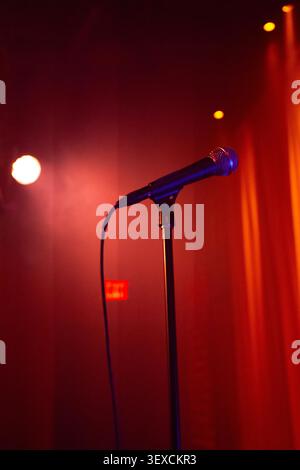 A dramatic cinematic view of a microphone on stage with a red curtain background, spotlights shining down. Stock Photo