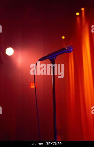 A dramatic cinematic view of a microphone on stage with a red curtain background, spotlights shining down. Stock Photo