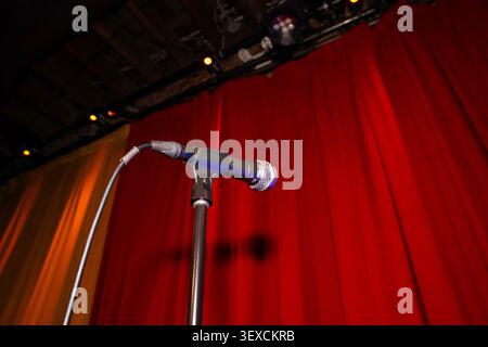 A dramatic cinematic view of a microphone on stage with a red curtain background, spotlights shining down. Stock Photo