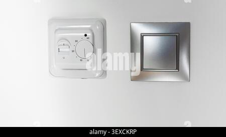 Mechanical room thermostat and modern light switch on wall Stock Photo