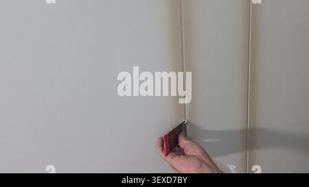 A close-up of a worker's hand using a metal spatula to apply joint compound to a seam on a wall. Stock Photo