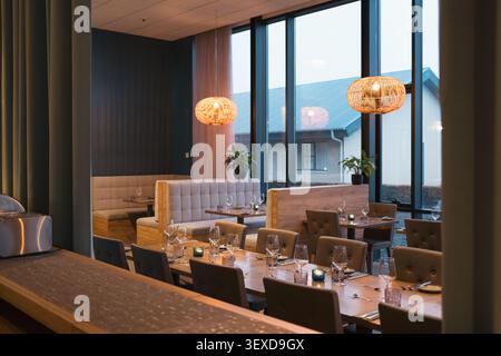Elegant dining table reservation setup with wooden table, comfortable seat, wine glass, cutlery, pendant lamps and arranged table ware Stock Photo