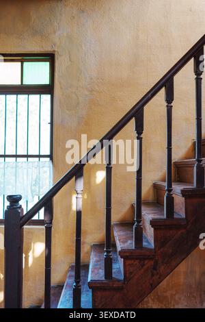 Old wooden staircase with rustic handrail and textured stain yellow wall and vintage window in chinese house Stock Photo