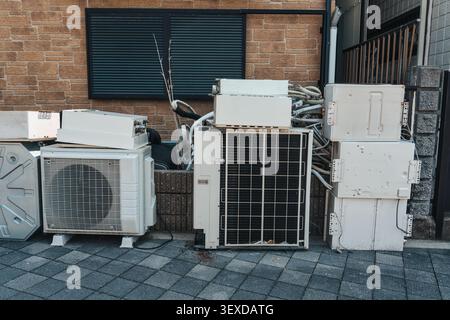 Damaged and used old air conditioner units, compressor, electrical components stacked beside residential building wall in urban Stock Photo