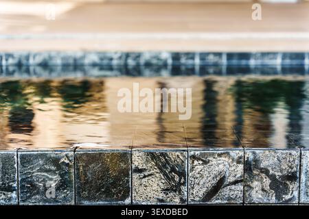 Closeup modern swimming pool edge with ripple water over dark stone tiles in luxury hotel Stock Photo