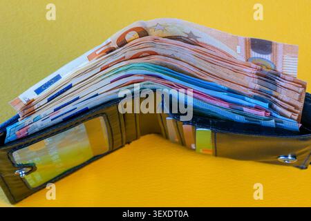Open black leather wallet filled with euro banknotes and payment cards on yellow background Stock Photo
