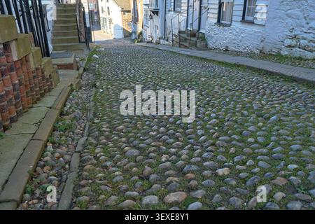 Detailed view of traditional rounded cobblestone road surface with stone walls and steps in a historic alleyway. Stock Photo