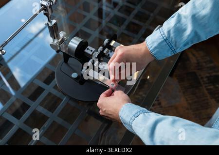 Man adjusting professional knife sharpener manual tool. Expert setting up precision blade sharpening device for maintenance. Metallic machine equipmen Stock Photo