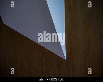 Abstract architectural detail featuring a sharp geometric white triangular element cutting into a warm brown wood paneled wall. Stock Photo
