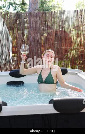 Luxury lifestyle concept with cheerful woman in hot tub, enjoying warm water, fresh air and a glass of white wine. Stock Photo