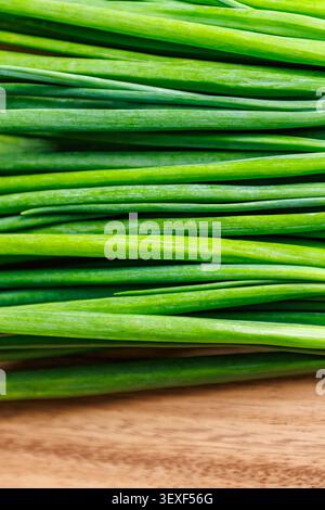 A detailed macro shot of fresh, vibrant green spring onion stalks laid horizontally on a wooden cutting board, serving as an organic food background. Stock Photo