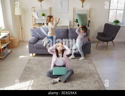 Mother working from home with naughty kids playing pillow fight game by couch Stock Photo
