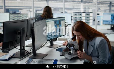 Woman using microscope in office, reviewing semiconductor substrate structures. Female materials scientists analyzing silicon wafer with optical device in industrial plant RD workspace, camera A Stock Photo