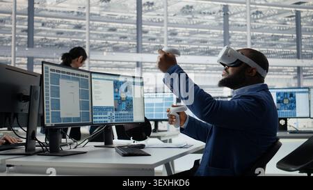 Microchip factory lab specialist using VR headset to analyze chip architecture. African american employee programming integrated circuits layout in office with virtual reality tech, camera A Stock Photo