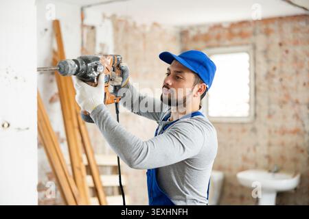Professional builder drilling hole in wall with perforator in repairable room Stock Photo