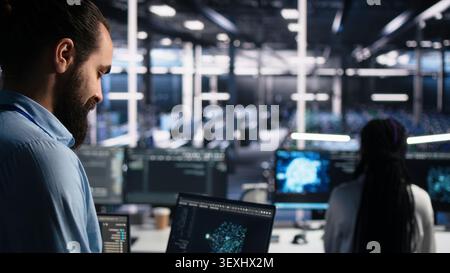 Computing facility software programmer working with notebook to track neural network working with AI large language model chatbot with working with AI on notebook to oversee servers powering machine. Stock Photo