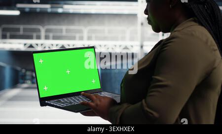Data center administrator uses green screen laptop in a data center to inspect hardware and maintain system stability. Stock Photo