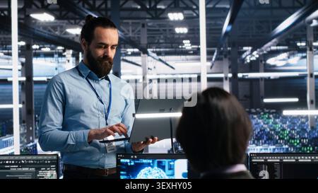 Data center technician uses laptop in a server room to monitor AI diagnostics and neural network performance. Stock Photo