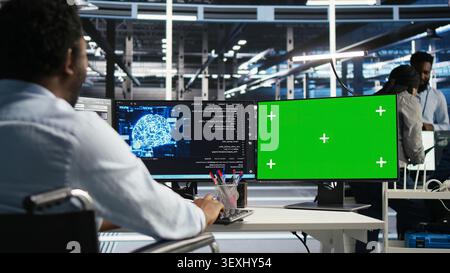 Computing facility technical specialist with paraplegia working with AI deep learning algorithms on chroma key computer to assess datasets while seated seated at chroma key computer using AI tools. Stock Photo