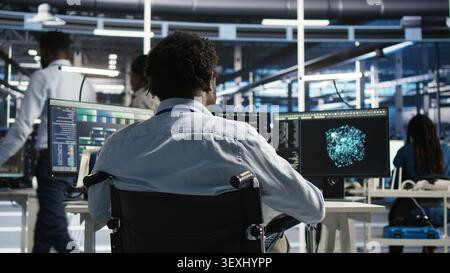 Server room software programmer with paraplegia interprets AI generated data analytics graphs, while man in wheelchair working with AI program showing predictive system metrics in server facility. Stock Photo
