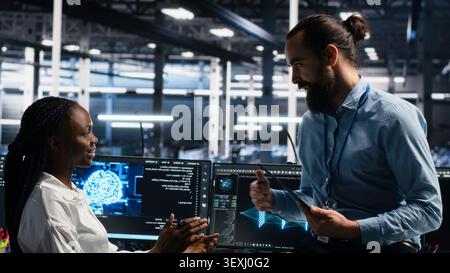Woman programs on a computer workstation in a data center with generative AI assistance. Stock Photo