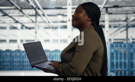 Smiling data center engineer uses a laptop after reducing downtime through disaster recovery planning. Stock Photo