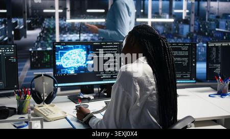 Female technician answers a phone call in a server hub, using an AI assistant to provide technical support to users. Stock Photo