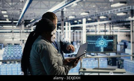 Data center colleagues use laptop deep learning tools in a server room to improve AI operations and system efficiency. Stock Photo