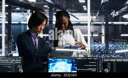 Data center engineers review paperwork while using deep learning algorithms to analyze datasets and recognize patterns in a server farm. Stock Photo