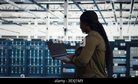African american IT professional manages software updates in a server room to keep data center systems stable. Stock Photo