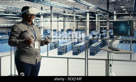 Data center engineer uses a VR headset in a server room to adjust AI systems and improve processing performance. Stock Photo