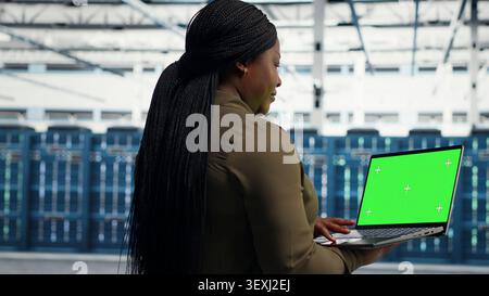 Data center technician uses an isolated screen laptop in a server room for editable AI infrastructure review. Stock Photo